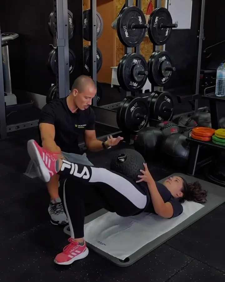 Personal trainer a orientar uma cliente num exercício de abdominais com bola medicinal no estúdio